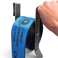 Hand holding the clip-on winder while a blue Cargo Control Center winch strap winds into a coil on it