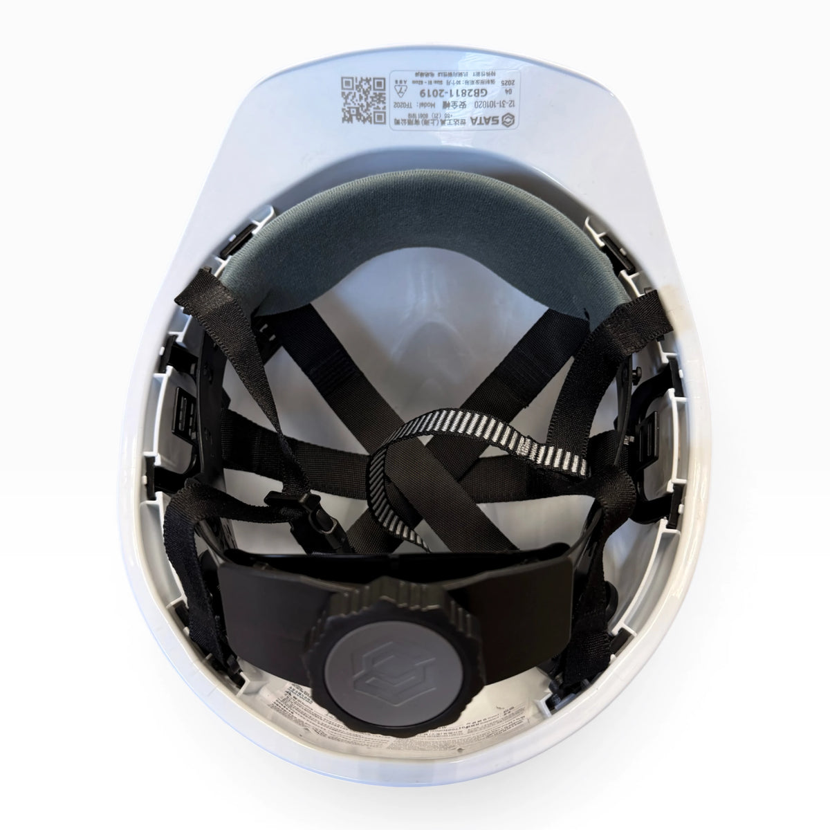 Underside of the hard hat showing the black suspension straps, grey brow pad, rear adjustment knob and a printed label.