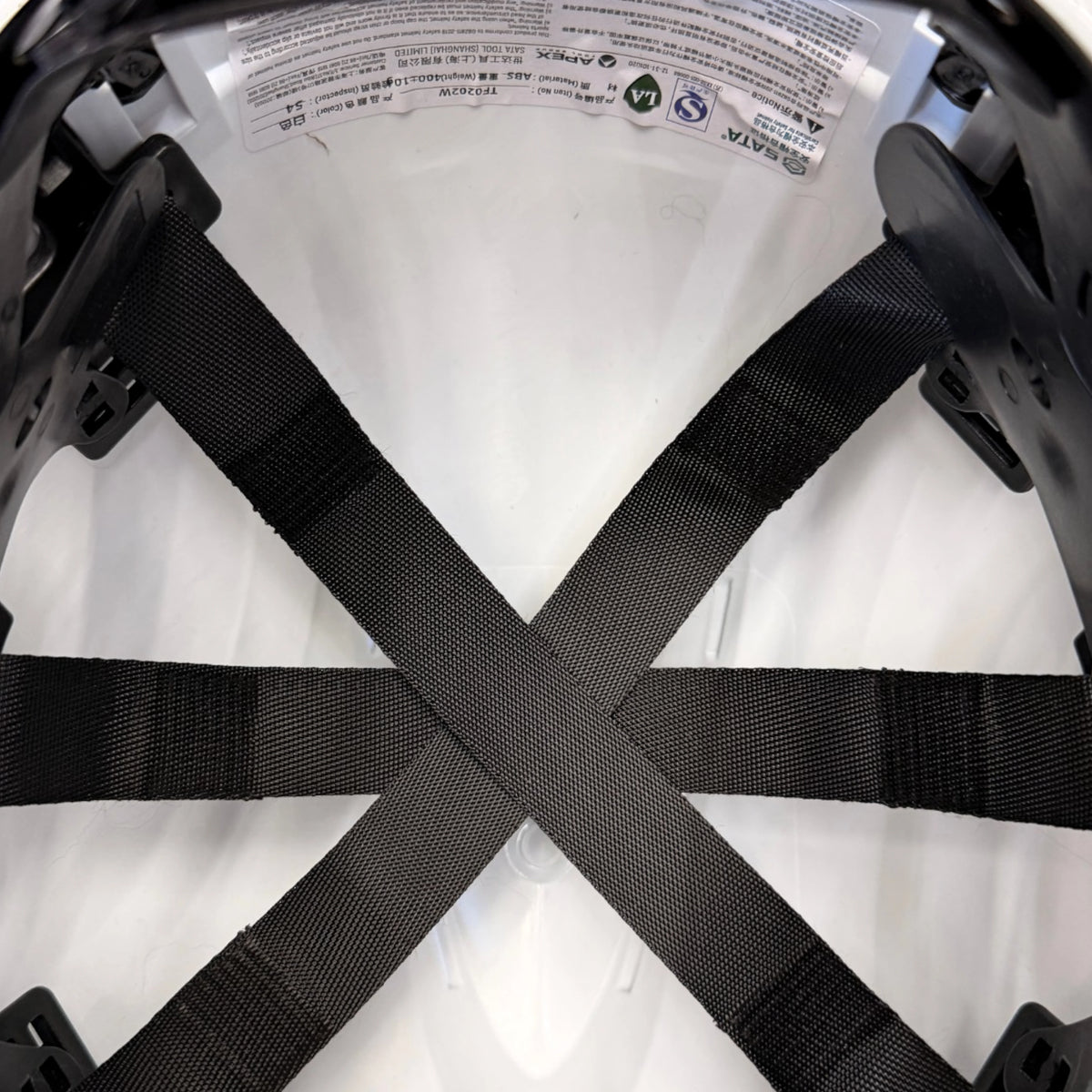 Three black suspension straps crossing inside the hard hat crown, with part of a printed label at the top edge.