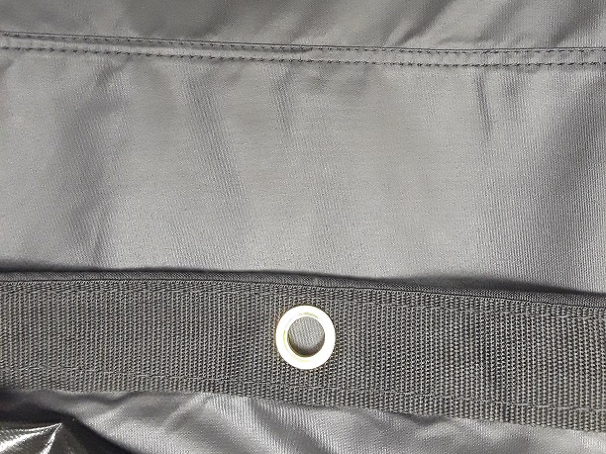 Black lumber tarp laid flat on white, seen from the long side with the end flap to the right and D-rings along both edges