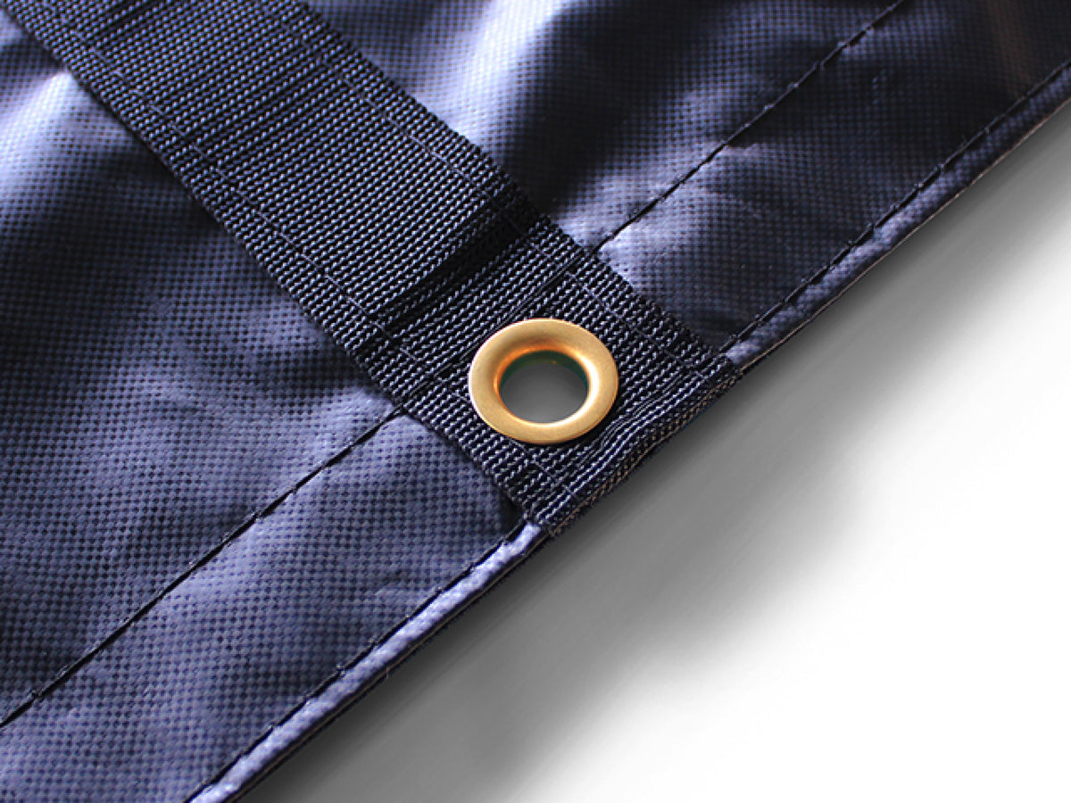 Brass grommet through the end of a black webbing strip at the tarp's double-stitched hem, close up